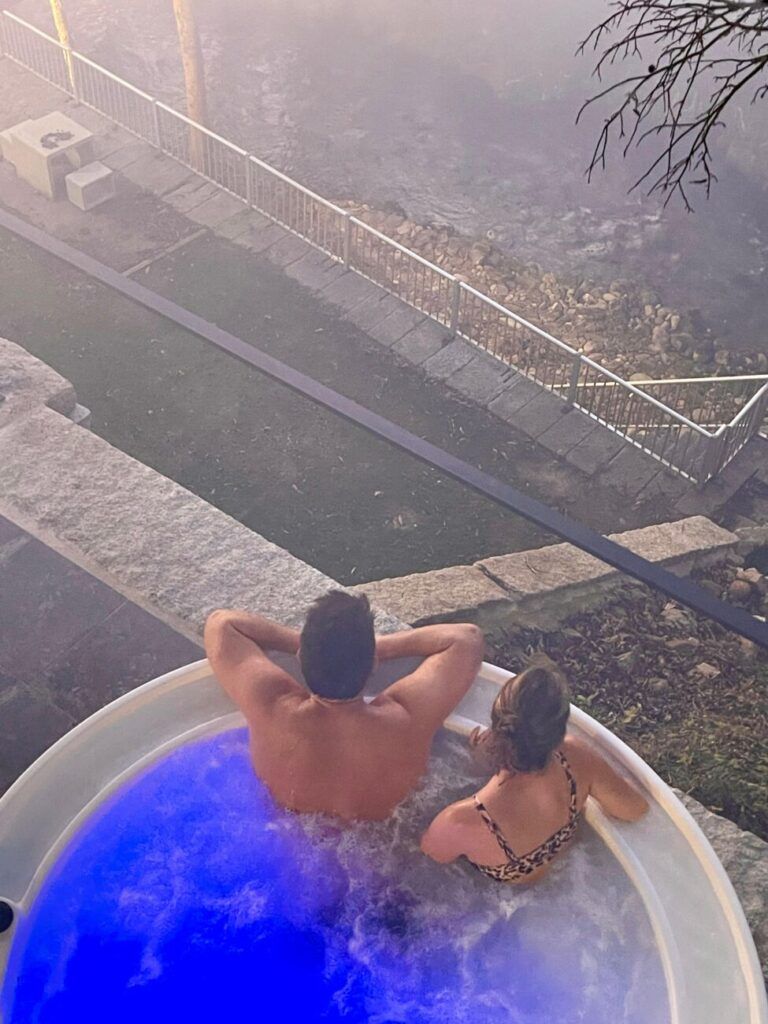 Pareja disfrutando del jacuzzi cubierto en la Villa Boutique 1880 durante un día de lluvia, con vistas al bosque de Gaxate.
