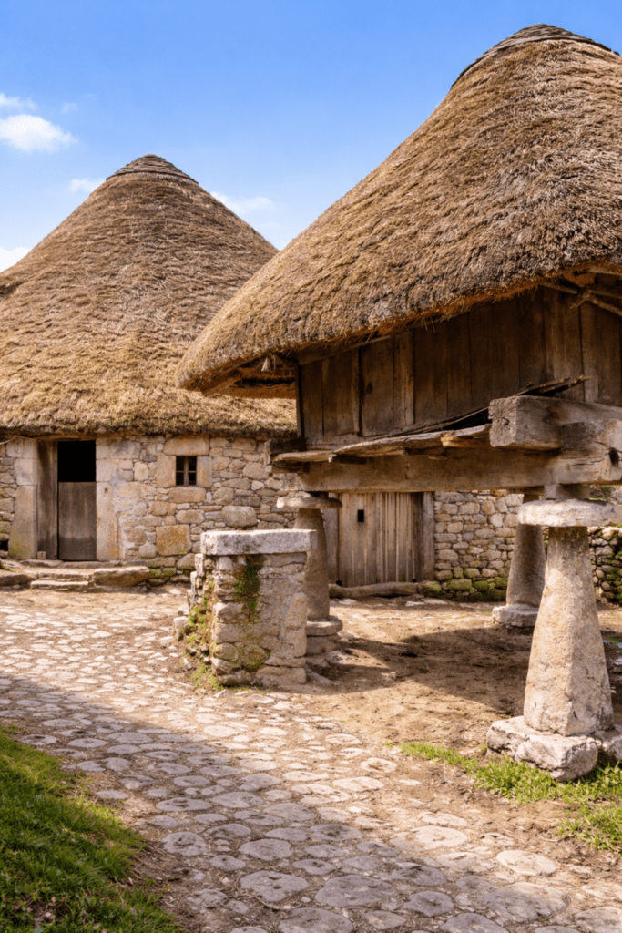 Palloza tradicional en Os Ancares (Lugo), con hórreo en lo que es la  arquitectura rural de montaña en un día soleado.”