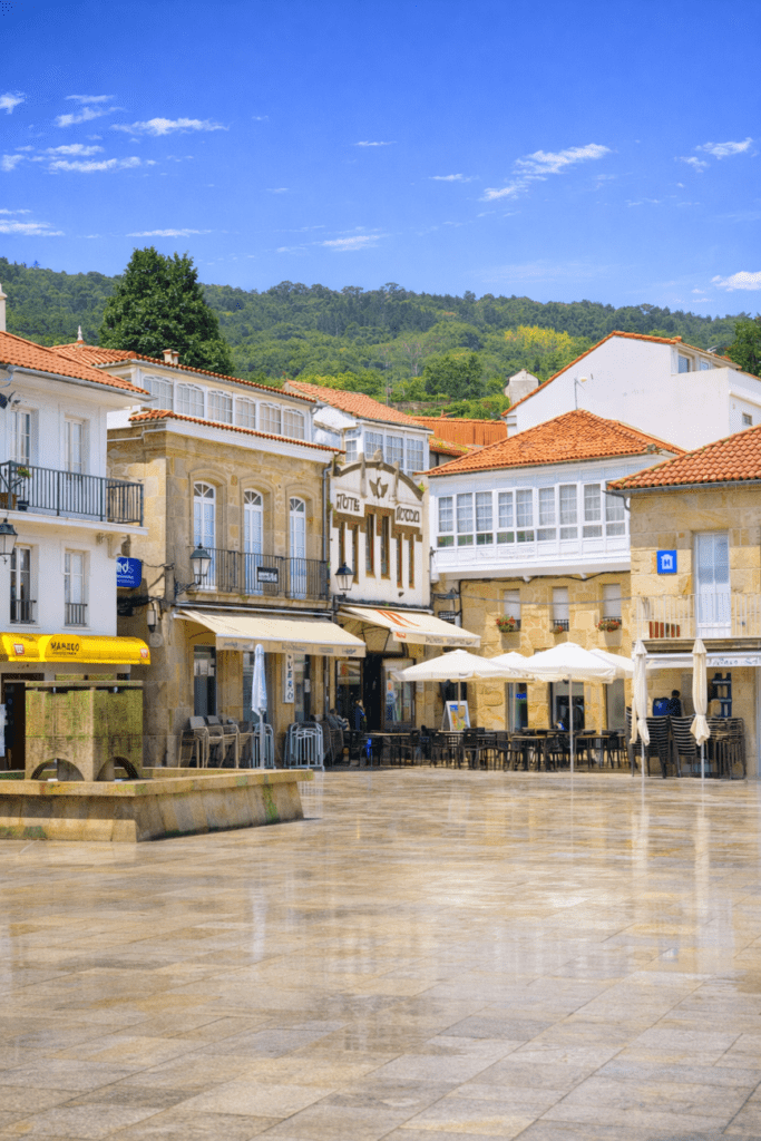 Plaza de Muros en A Coruña con casas tradicionales de piedra, terrazas y ambiente marinero en un día soleado.