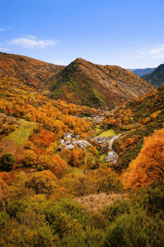 Paisaje de la Ribeira Sacra en Galicia en un día soleado, con valle montañoso, bosque otoñal y pequeño pueblo entre montañas.