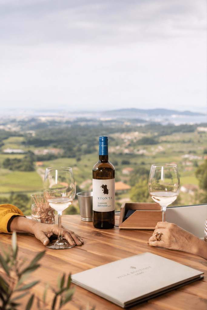Botella de albariño y copas de vino sobre una terraza con vistas panorámicas al paisaje verde de Galicia desde Villa Boutique 1880