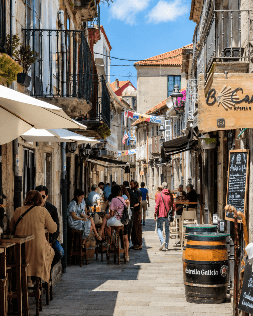 Terrazas y ambiente animado en una calle histórica de Baiona, con bares de piedra gallega, balcones tradicionales y visitantes disfrutando del casco antiguo.