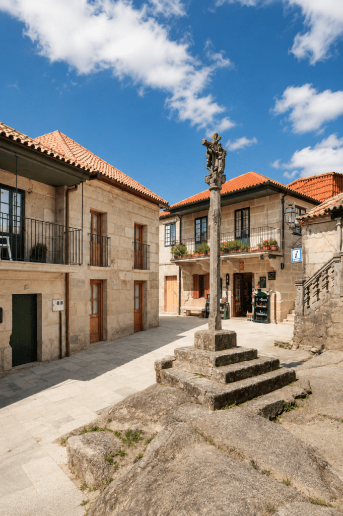 Plaza histórica de Combarro con cruceiro de piedra y casas tradicionales gallegas restauradas bajo un cielo azul en las Rías Baixas.