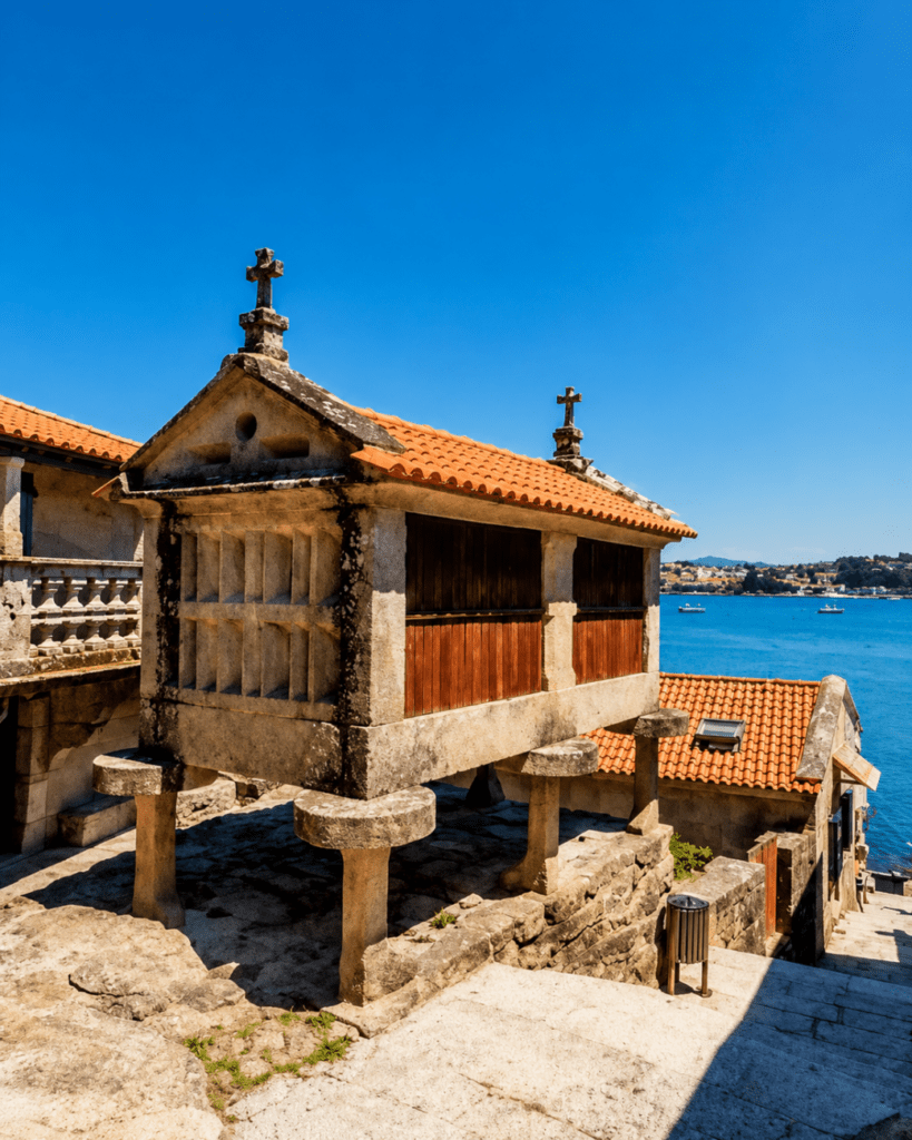 Hórreo tradicional de piedra en Combarro con vistas a la ría, tejados de teja y el mar azul de las Rías Baixas en un día soleado.