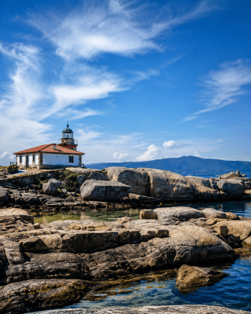 Faro de Punta Cabalo en A Illa de Arousa, situado junto a rocas de granito y aguas tranquilas de la ría de Arousa.