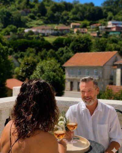 Pareja disfrutando de una copa de vino con vistas a los bosques y al río en Villa Boutique 1880, en Gaxate, A Lama.
